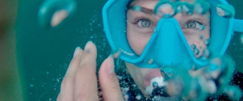 Mujer con gafas de buceo rodeada de burbujas de agua.